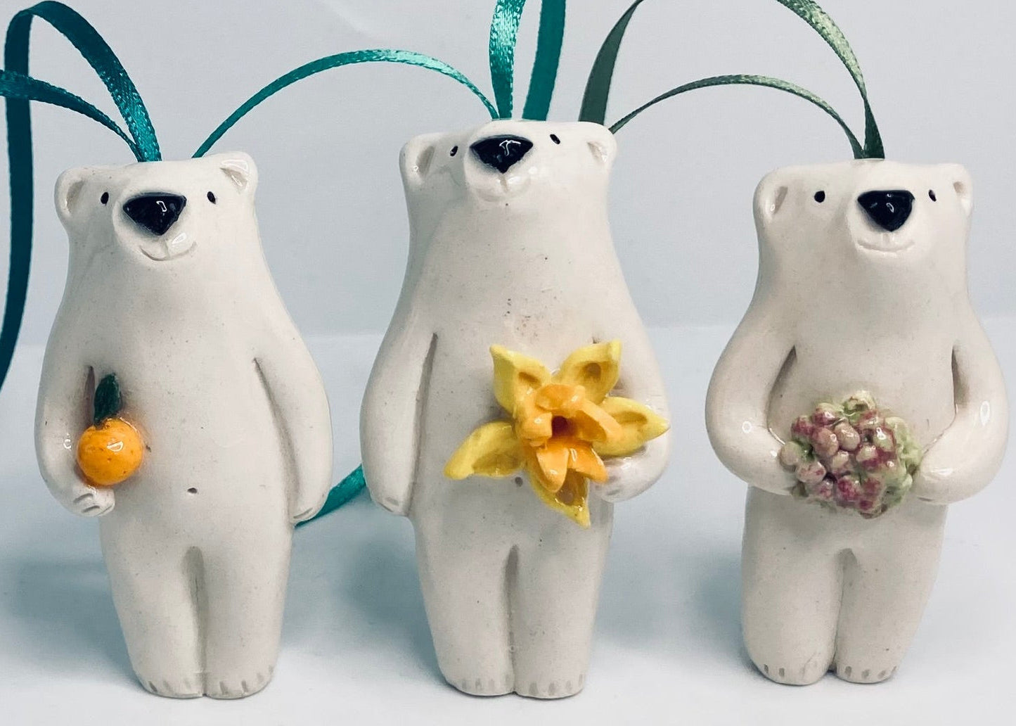 Three ceramic polar bear ornaments holding flowers on a light gray background